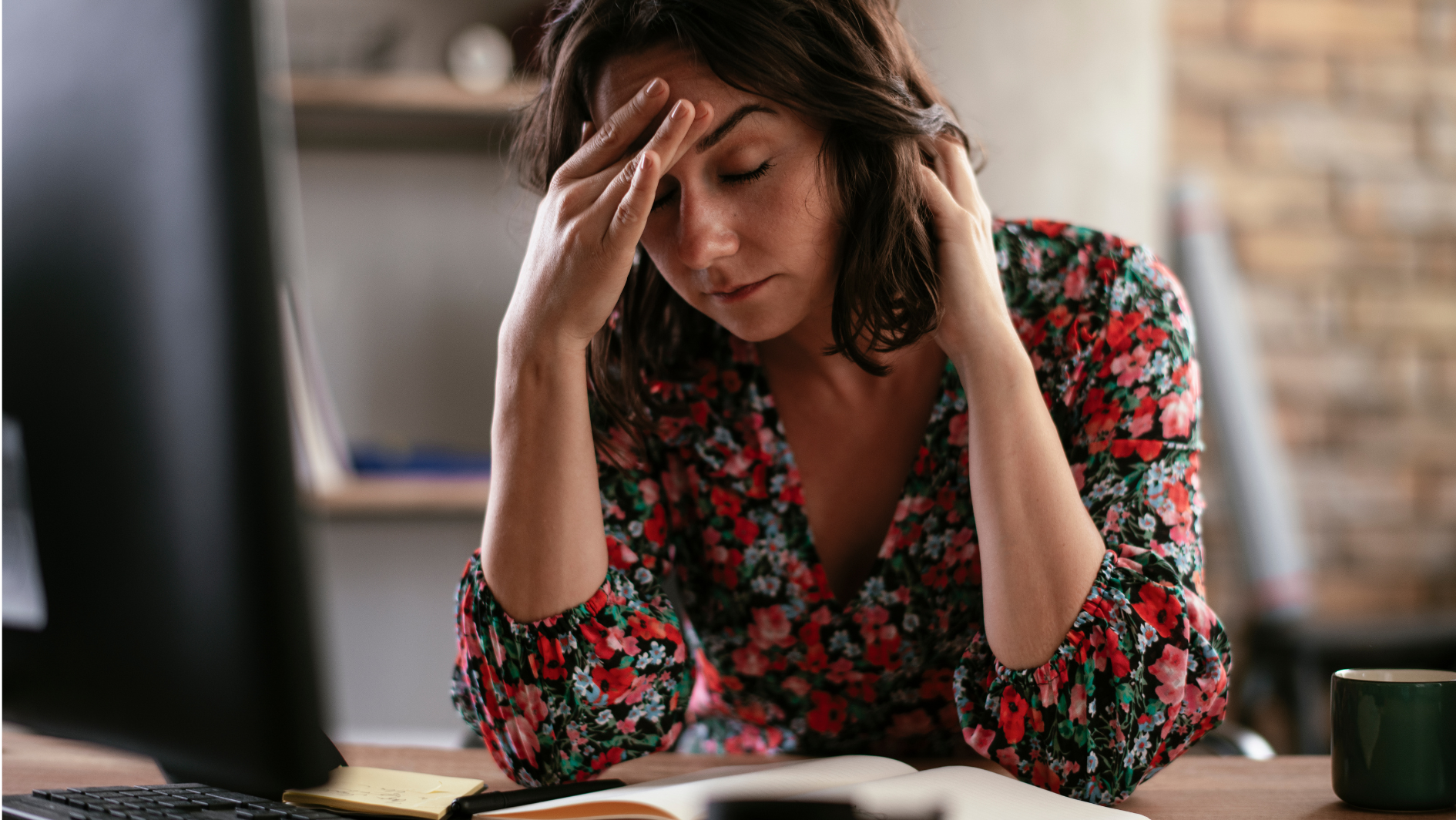 a woman in floral attire at her desk experiencing head pain, need migraine relief during the Christmas season