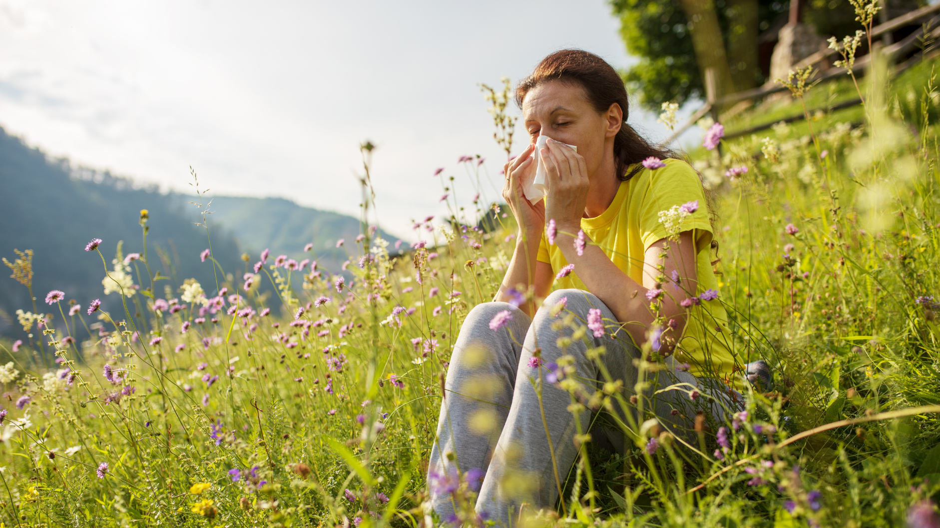spring allergies and migraines, woman suffering from seasonal allergies in a field, blowing her nose